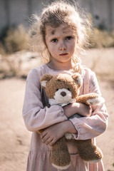 cute kid with dirty face looking at camera while holding teddy bear, post apocalyptic concept
