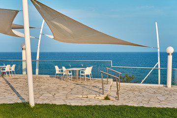 Restaurant terrace of a hotel with white tables and chairs. Sea coast, white stone cape in Kalymnos...