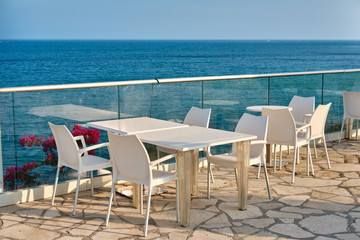 Restaurant terrace of a hotel with white table and chairs. Sea coast, white stone cape in Kalymnos island or Governor Beach in Cyprus.