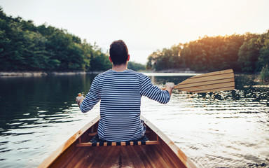 Man in sailor shirt paddling canoe on the sunset lake	
