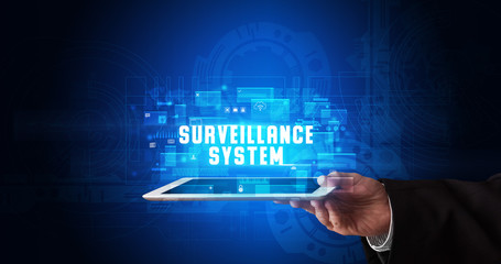 Young business person working on tablet and shows the digital sign: SURVEILLANCE SYSTEM