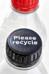 Plastic bottles and black and red bottle caps with please recycle message against a white background. Concept of plastic pollution. Vertical image.	