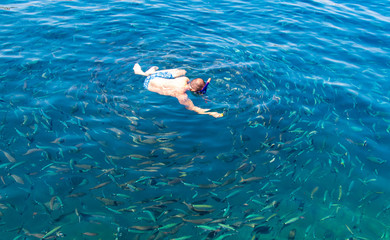 A man swims in the blue water of the sea