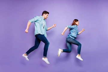 Obraz na płótnie Canvas Full size profile side photo of cheerful funny funky spouses jump run after discounts enjoy spring summer holidays wear denim jeans outfit white sneakers isolated over violet purple color background