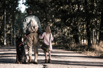 back view of man holding hands with kid near german shepherd dog, post apocalyptic concept