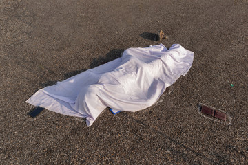 Concept of road accident scene, High angle view of chalk outlined dead body covered under white...
