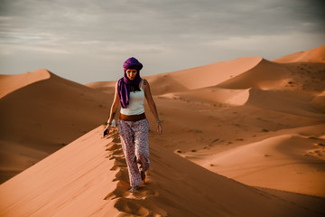 Tourist woman wearing a purple turban walking on a desert dune