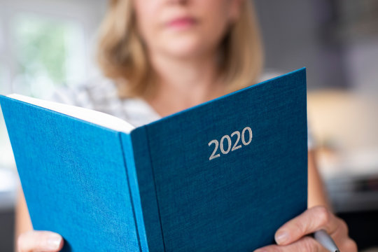 Close Up Of Woman Opening New Year 2020 Diary On Table At Home
