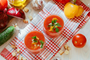 Obraz na płótnie Canvas Tomato soup gazpacho in glass with herbs and ingredients on the kitchen. A beautiful summer soup spilled in glasses surrounded by juicy vegetables.