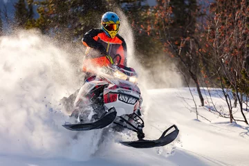 Fotobehang the guy is flying and jumping on a snowmobile on a background of winter forest  leaving a trail of splashes of white snow. bright snowmobile and suit without brands. extra high quality © Wlad Go