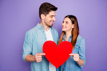 Fototapeta na wymiar Portrait of romantic lovely spouses students hold paper card red big heart sign of their romance enjoy date 14-february holidays wear denim jeans shirt isolated over purple violet color background