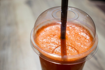 Cold fresh carrot and orange juice in a plastic glass on wooden table