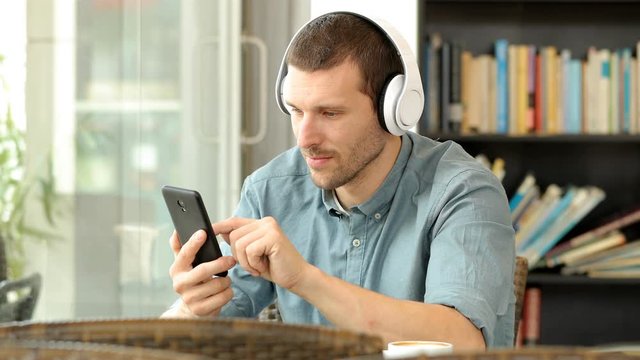 Serious man wearing headphones listening to music on mobile phone sitting in a bar