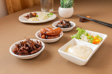 Insect food collection for fried Cricket, Grasshopper and Worm with vegetable salad in the white bowl on the table. Healthy meal high protein diet concept.