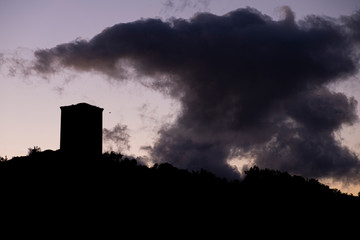 Silueta a contraluz de una torre medieval y una gran nube oscura en la puesta de sol. A Limia, Ourense. Galicia. España.