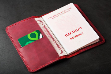 Red handmade passport cover made of genuine leather on a dark background, revealed with a passport and a green electronic card
