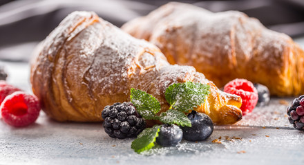 Freshly crispy croissants sprinkled sugar powder with raspberry blackberry and blueberry with mellisa leaves