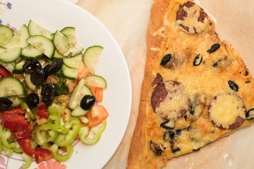 Vegetable salad on a plate and a slice of pizza