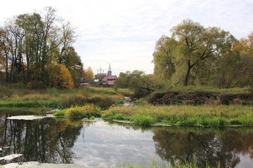 Fototapeta na wymiar river in the village Dunilovo with church, houses, trees in autumn bright day