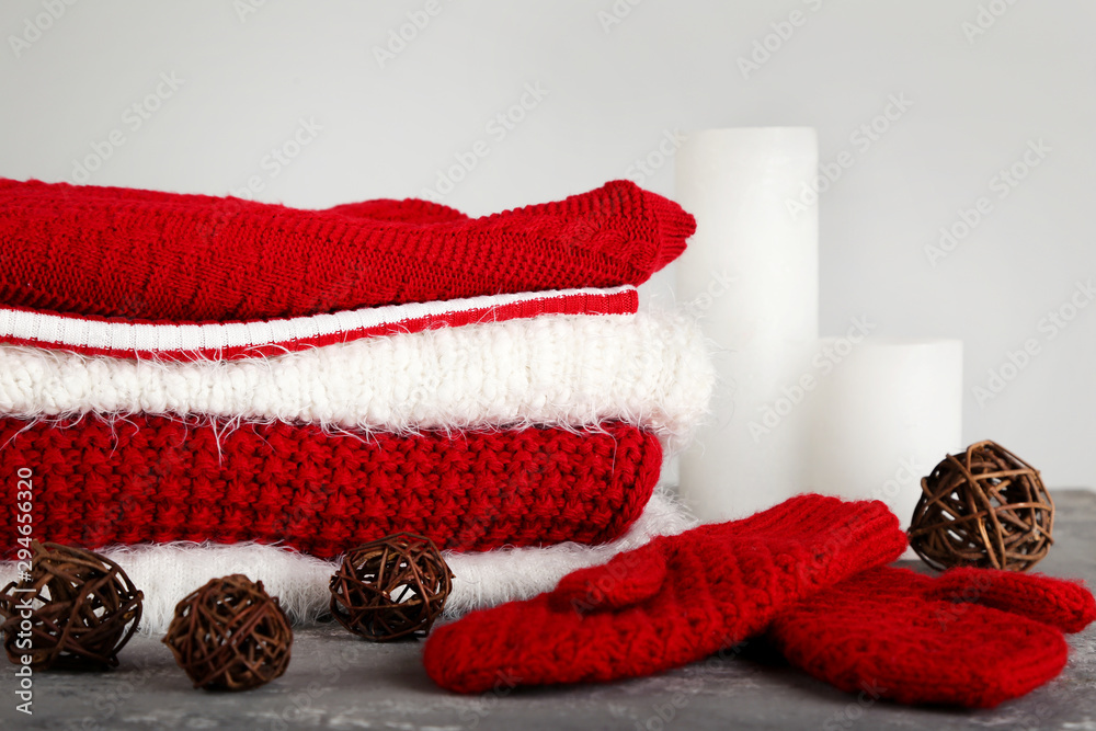 Sticker Folded knitted sweaters with pair of gloves and candles on grey background