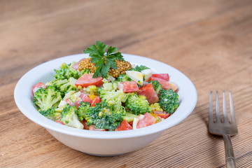 Delicious salad with broccoli, tomato, onion and boiled egg with cream sauce in plate on wooden background. Healthy food