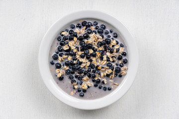 Oatmeal with fresh blueberry, almond milk and honey for breakfast in plate on wooden background. Rustic style. Top view.
