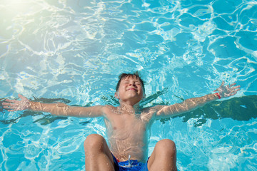 Portrait of cheerful European boy swimming in pool. He is enjoying his summer vacations.