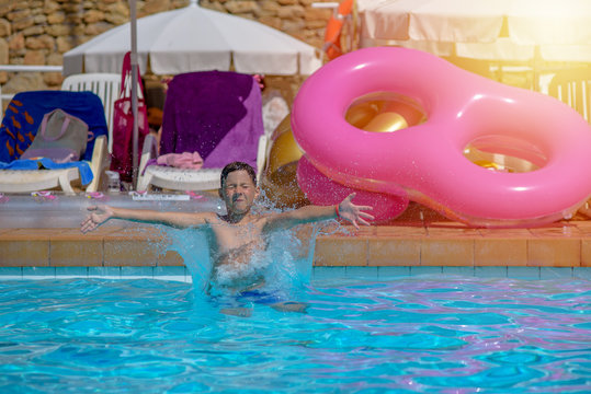 Boy having fun making fantastic jump into swimming pool on summer vacations. His arms are wide open.
