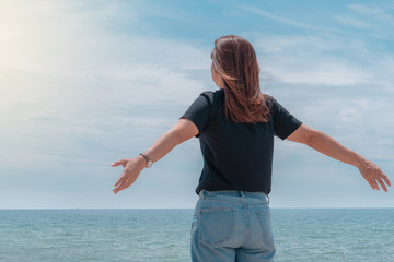 Young woman stand relaxed on beach with arms open to the sea looking