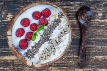 Smoothie in coconut bowl with raspberries, oatmeal, sunflower seeds and chia seeds for breakfast , close up. The concept of healthy eating, superfood