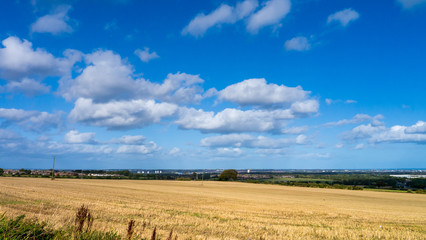 Fototapeta na wymiar Recently harvested field set against a beautiful blue sky with white clouds with the City of Sunderland in the distance. Taken on a warm autumn day.
