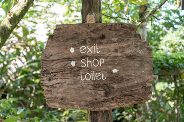 Text exit, shop and toilet on a wooden board in a rainforest jungle of tropical Bali island, Indonesia. Exit, shop and toilet wooden sign inscription in the asian tropics