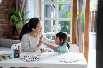 mother and daughter high five during learing to read and write together at home
