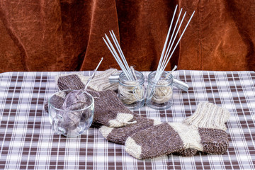 Handmade knitted socks, skeins of yarn and needles in a mug and jars on the table