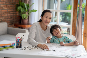 smiling happy mother and daughter looking at camera while learning together at home