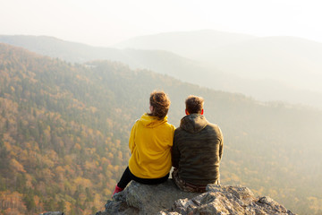 Couple in love sitting at the top of the mountain and watching autumn landscape. Sunset