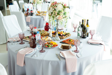 A wedding table for guests decorated with flowers and a tablecloth in a designer style with food and drinks. Decor and design of events, catering.