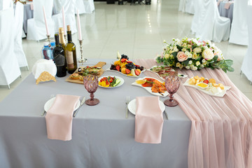 A wedding table for newlyweds groom and bride decorated with flowers and a tablecloth in a designer style with food and drinks. Decor and design of events, catering.