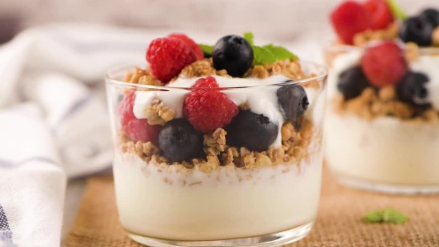 Granola blackberries and raspberries homemade yogurt in glass on light white wooden background. Healthy food concept.