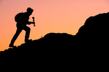 silhouette of a traveler walking with a backpack on the mountains in the camera and tripod