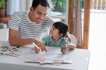 happy asian father teaching letter to her daughter at home. read and write lesson