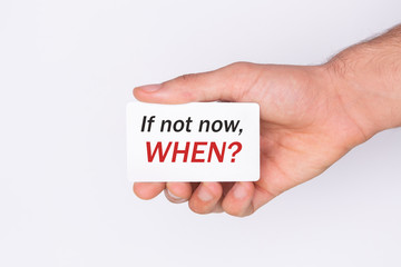If not now, when?The hand holds a card with the inscription. White background. Copy space
