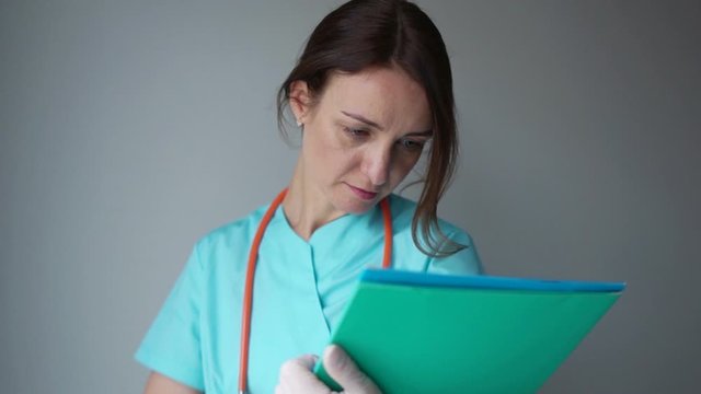 Portrait of young female doctor showing something or copyspase for product or sign text, with blue foder, over grey background. International Doctor's Day, medicine and healthcare concept