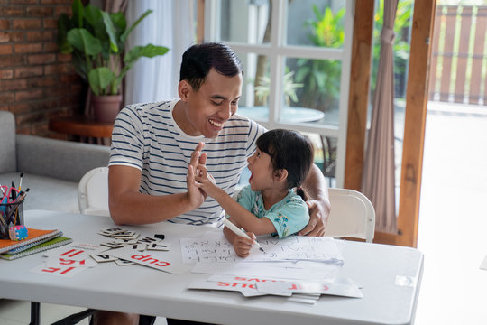 portrait of father and daughter high five while studying at home together