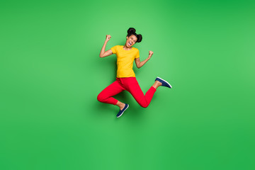Fototapeta na wymiar Full size photo of pretty dark skin lady jumping high celebrating exciting victory raising fists wear casual yellow t-shirt red pants isolated green background
