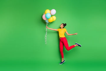 Full body profile photo of pretty millennial dark skin lady holding air balloons going to fly up in sky wear casual yellow t-shirt red pants isolated green background © deagreez