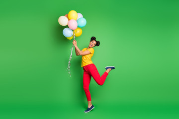 Full length photo of pretty millennial dark skin lady holding air balloons going to fly up in sky wear casual yellow t-shirt red pants isolated green background