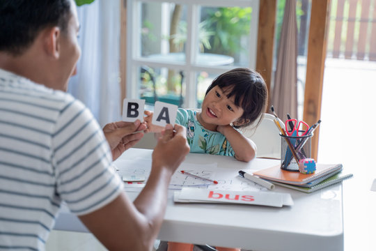 portrait of father teaching toddler how to read by using simple word and letter on a flash card at home