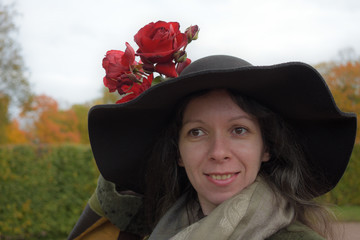 young beautiful pretty lady woman posing in a long green and brown dress gown overcoat walks in the garden of the palace in Oranienbaum near Saint Petersburg, Russia and plays with late autumn roses