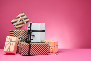 Different sizes, colorful, striped and plain paper gift boxes tied with ribbons and bows on a pink surface and background. Close-up, copy space.
